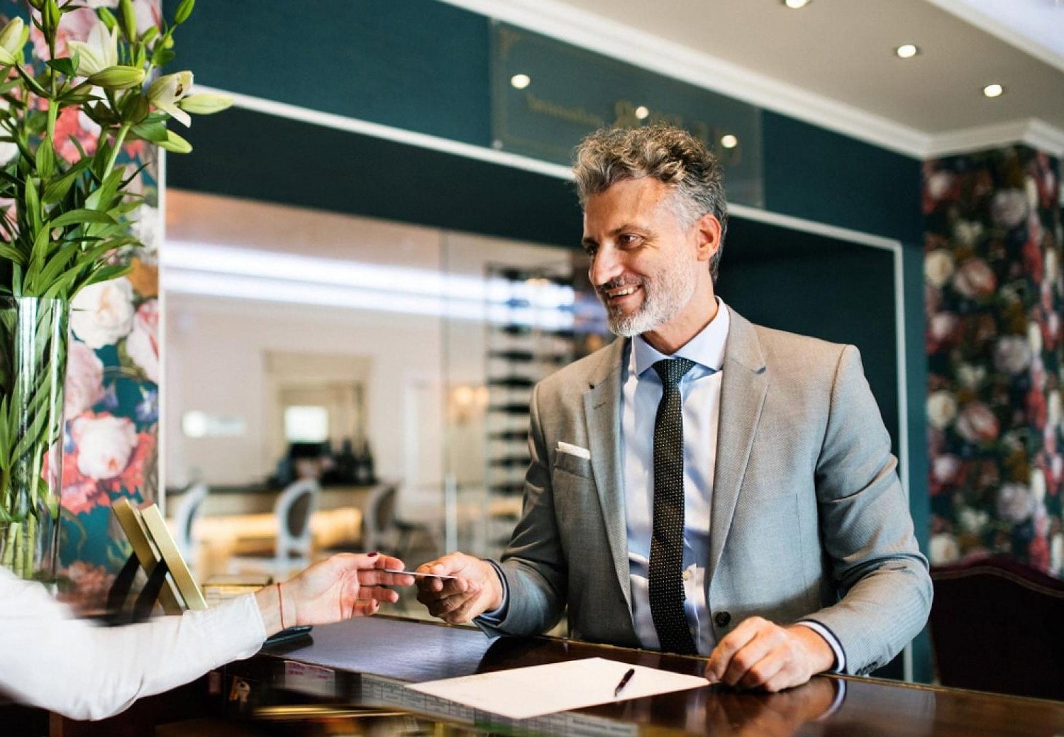 Hotel concierge in a grey suit handing a key card to a guest at the front desk