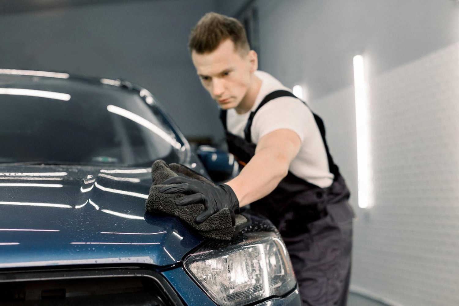 Detailer wiping a dark blue car bonnet with a microfibre cloth inside a UAE studio