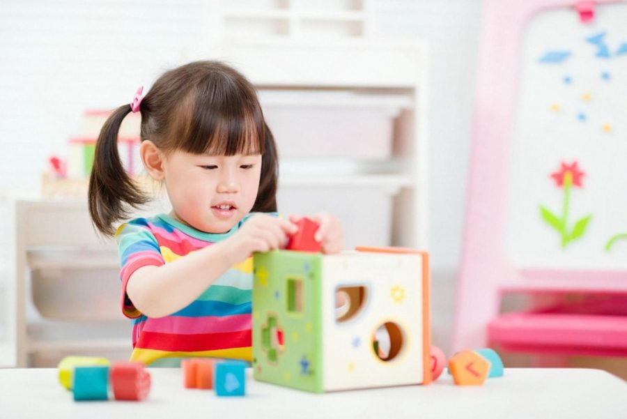 Toddler girl playing with a wooden shape-sorter educational toy at a table