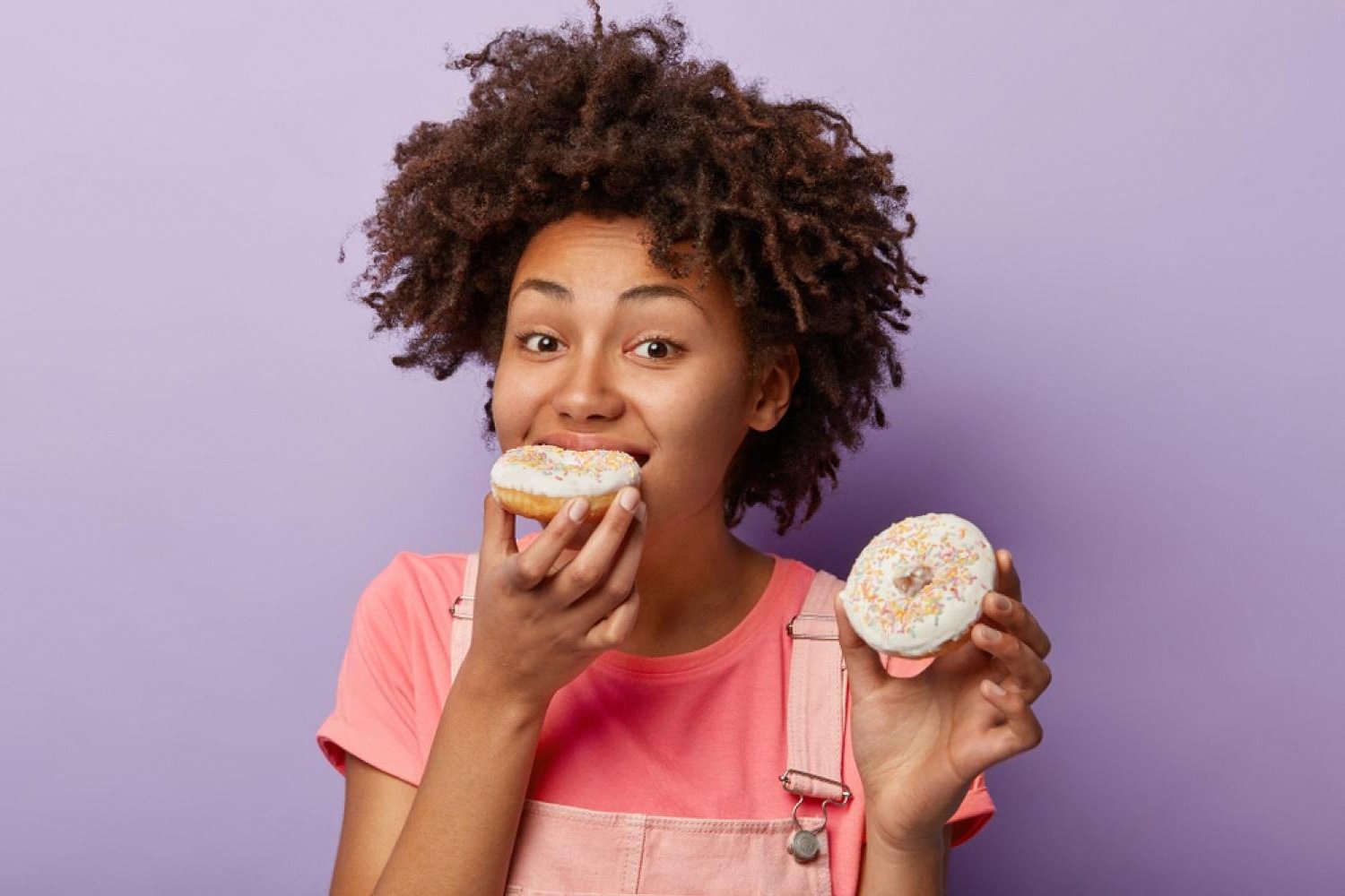 Young woman holding sugary doughnuts, an example of sticky sweets to avoid while wearing braces
