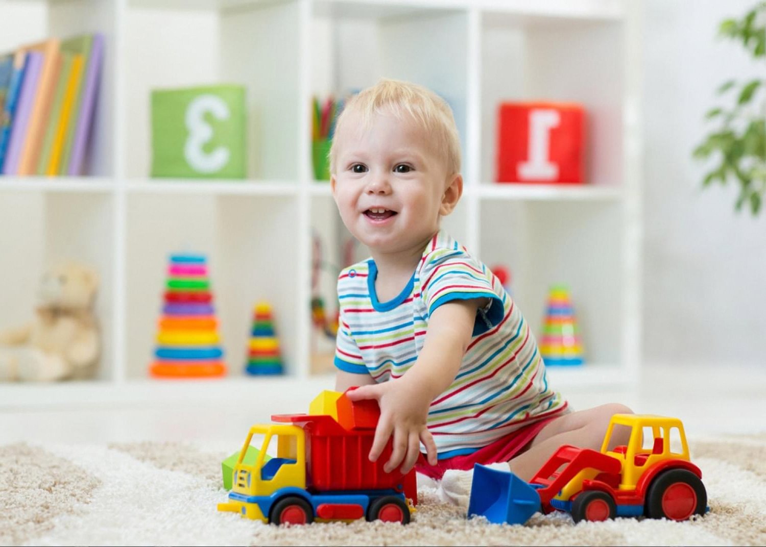 Smiling baby boy sitting on a rug playing with colourful learning toys in a bright playroom