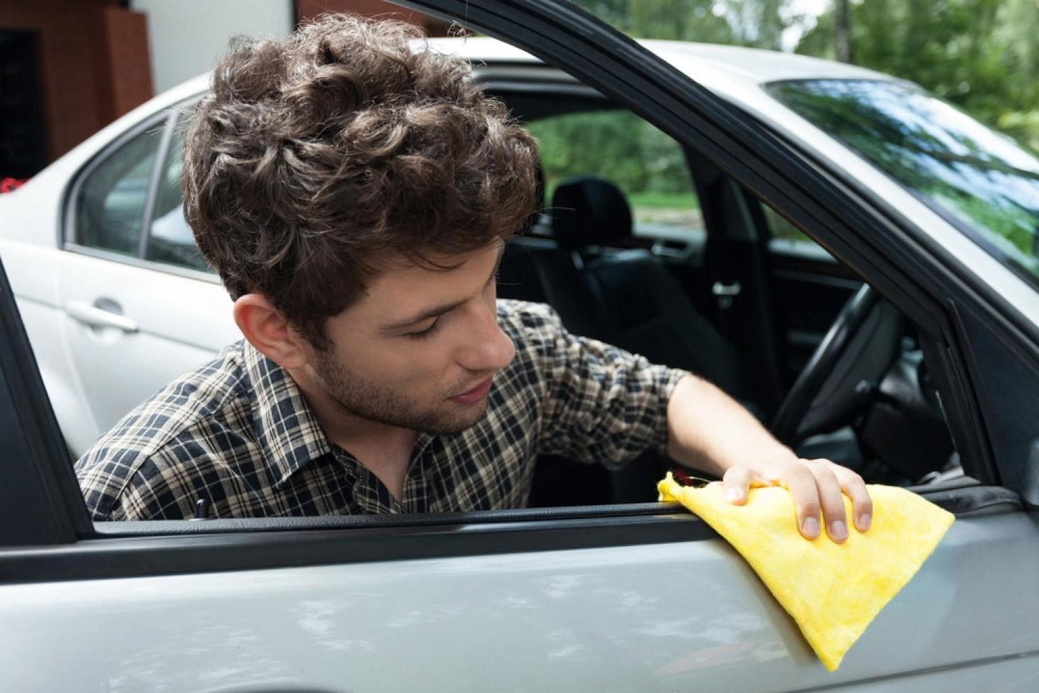 Young owner cleaning the door of a used silver sedan with a yellow cloth