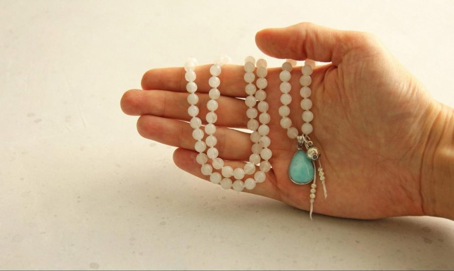 A hand holding a delicate pearl necklace with a turquoise pendant, the kind of piece often stored in a small home jewelry safe