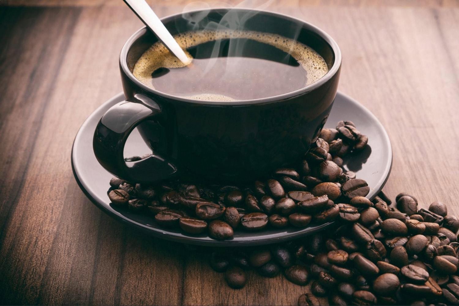 Black cup of freshly brewed specialty coffee with roasted beans on a wooden table